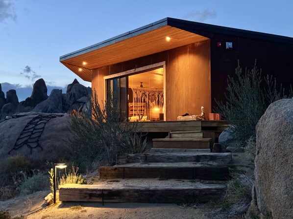 A modern building with a wooden exterior and a glass entrance, situated in a rocky landscape.