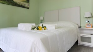 Ein ordentlich bezogenes Bett mit weißen Leinen und einem Strauß gelber Rosen.