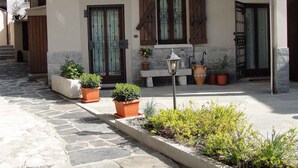 Un edificio con entrada empedrada de piedra, contraventanas de madera y plantas en macetas.