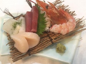 A plate with various seafood items including shrimp, fish, and possibly other seafood, arranged on a woven mat.