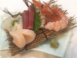 Um prato com diversos frutos do mar, incluindo camarão, peixe e possivelmente outros, disposto sobre um tapete trançado.