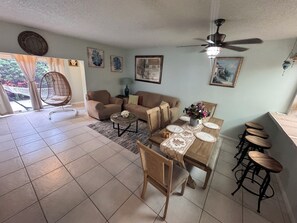A living room with a sofa, a dining table with chairs, a hanging chair, and a ceiling fan.