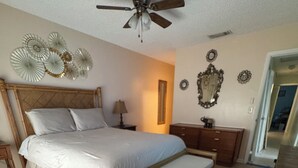 Un dormitorio con una cama de madera, un banco, ventilador de techo y espejos decorativos en la pared.