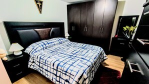 A bedroom with a bed, a nightstand, a dresser, a mirror, and a wall-mounted cross. - Complete Apartment in Coapa CDMX (Ciudad de México)