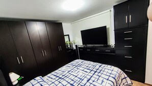 A bedroom with a bed, dark wooden wardrobe, a flat-screen TV, and a desk with a lamp. - Complete Apartment in Coapa CDMX (Ciudad de México)
