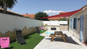 A backyard with a swimming pool, a wooden fence, and a patio area with a table and chairs. - Gîte de Leni (Torreilles)