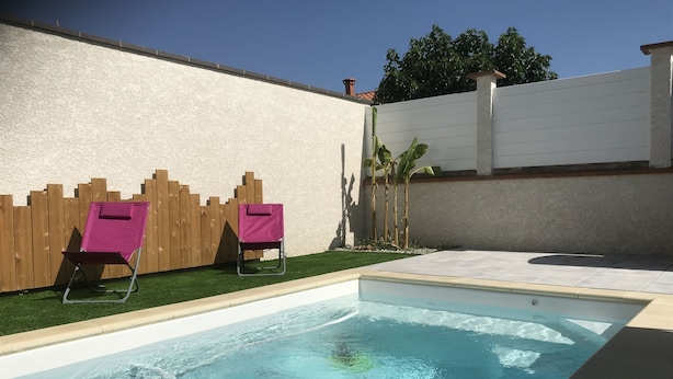 A swimming pool with two pink lounge chairs and a wooden fence. - Gîte de Leni (Torreilles)