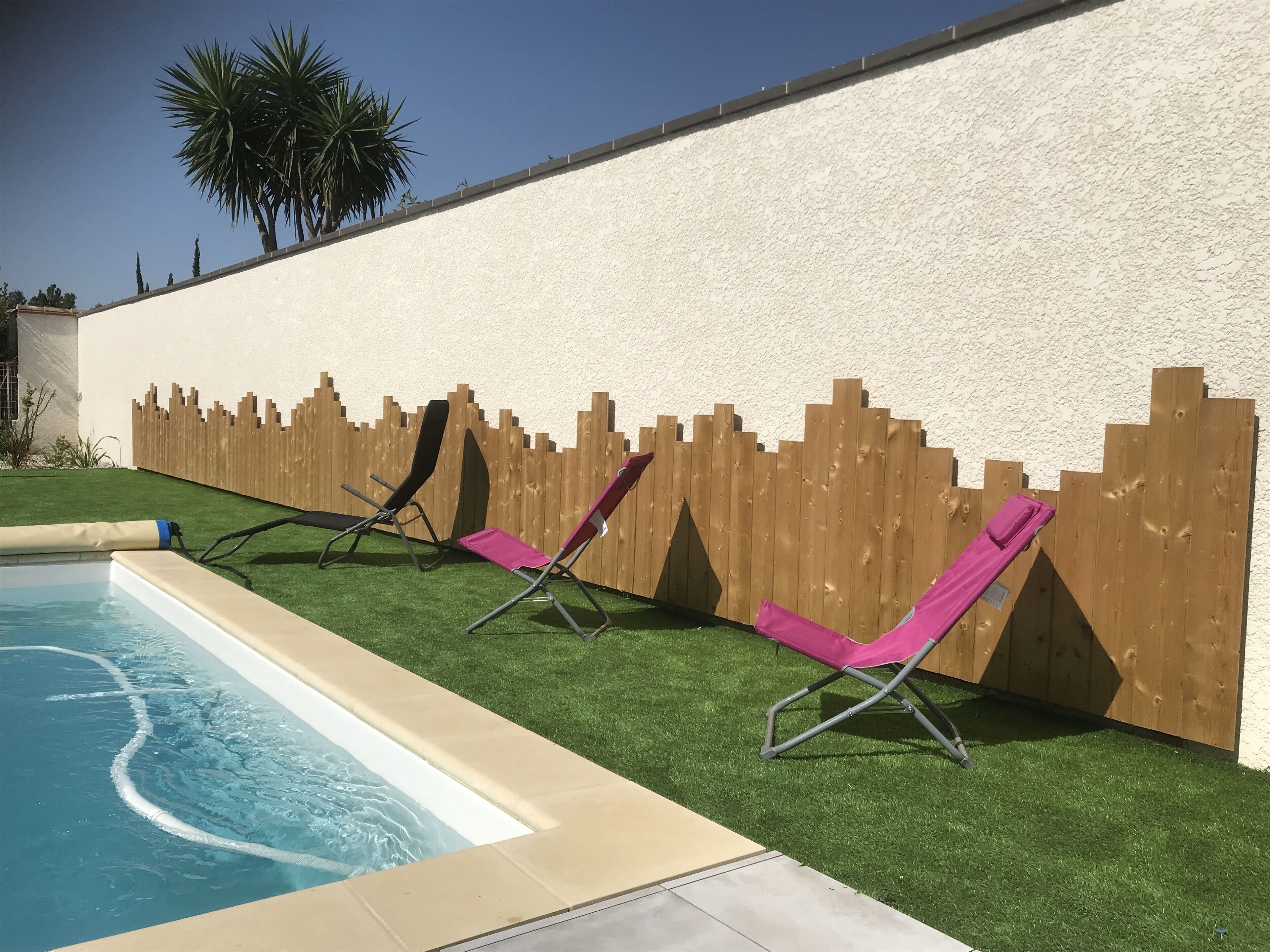 Une piscine avec deux chaises longues et une clôture en bois.