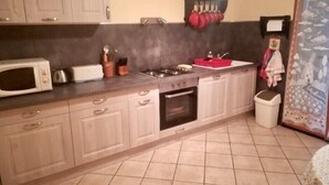 A kitchen with a microwave, toaster, stove, oven, and a sink with a red mat. - Gîte de Leni (Torreilles)