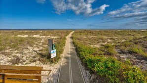 Ein Weg, der zu einem Strand mit einer hölzernen Bank und Hinweisschildern führt.