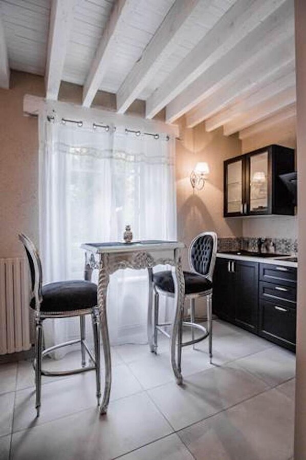 Une cuisine avec des meubles blancs, une table à manger avec des chaises et une fenêtre avec des rideaux.