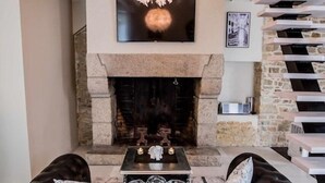 Un salon avec une cheminée, un canapé en cuir noir et un luminaire suspendu.