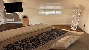 Une chambre à coucher avec un lit, une table de chevet, une télévision, un néon et un ventilateur sur pied.