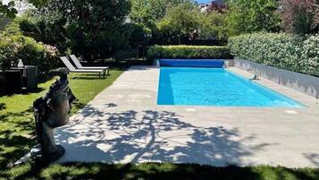 A swimming pool with a clear blue water, surrounded by a well-maintained garden and a statue.