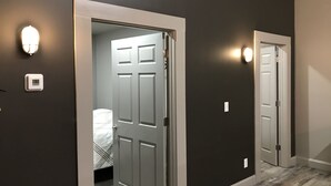 Un couloir aux murs sombres, aux portes blanches, avec un lit visible au fond.