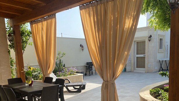 An outdoor patio with a wooden pergola, covered tables and chairs, and a view of a building in the background. - Villa Sole (San Pietro In Bevagna)