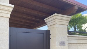 A closed dark-colored metal gate with a stone pillar and a sign above it. - Villa Sole (San Pietro In Bevagna)
