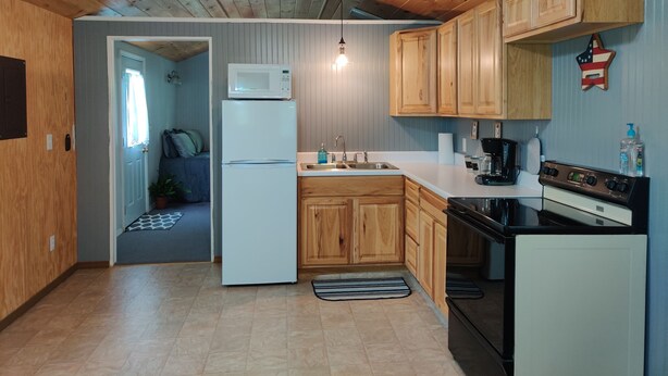 A compact kitchen with wooden cabinets, a white refrigerator, a stove, and a microwave. - Tiny House on the Farm: Watch Farm Animals, Near Buffalo River (Western Grove)