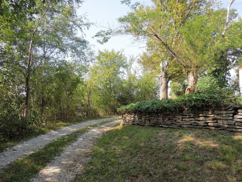 A gravel path leading through a wooded area with a stone wall on one side.