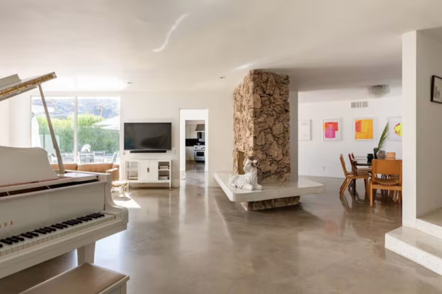 A spacious living room with a piano, a stone fireplace, a television, and a dining area with chairs and a table.