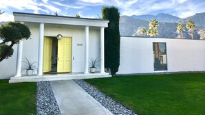 Une maison moderne avec une porte jaune, le numéro 2065, des colonnes blanches et une pelouse bien entretenue.