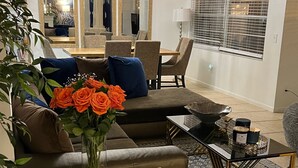 Una sala de estar moderna con un sofá, una mesa de centro y un puf azul. Hay un florero con flores sobre la mesa de centro.