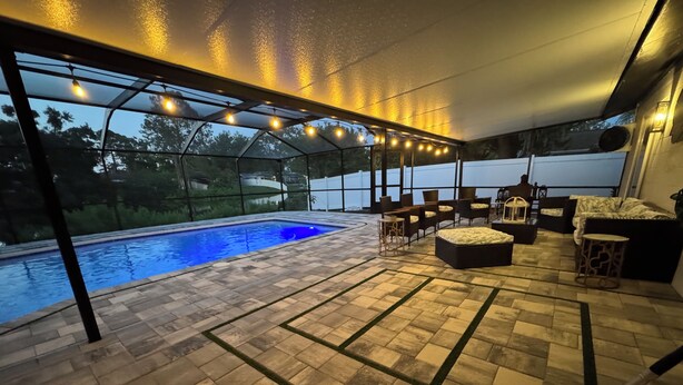 Un patio exterior con piscina, luces colgantes y mobiliario de exterior.