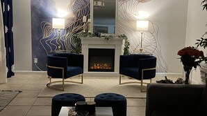 Una sala de estar moderna con chimenea, dos sillones azules, una mesa de centro y una pared decorativa con patrones abstractos.
