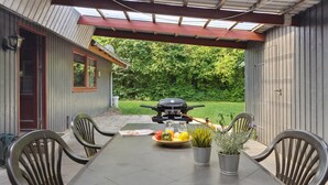 A covered patio with a table set for four, a grill, and a view of a green lawn. - 4 bedroom beautiful home in Hemmet (Hemmet)