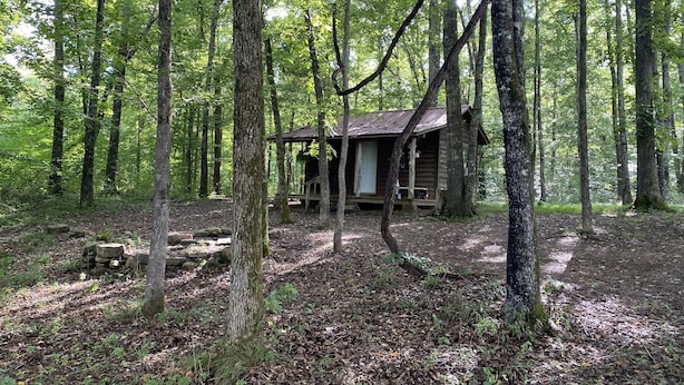 Eine rustikale Holzhütte in dichtem Wald mit einer Holzterrasse und einer Veranda.