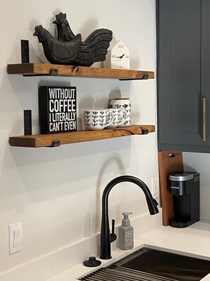 Modern kitchen with a minimalist design, featuring a shelf unit with decorative accents and a coffee maker.