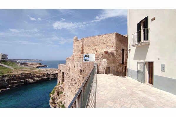 Un bâtiment situé sur la côte, doté d’une façade en pierre, d’un balcon avec une rambarde en métal et offrant une vue sur la mer.