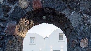 Un arco de piedra que da acceso a un edificio blanco con una escalera y una barrera de cuerda.