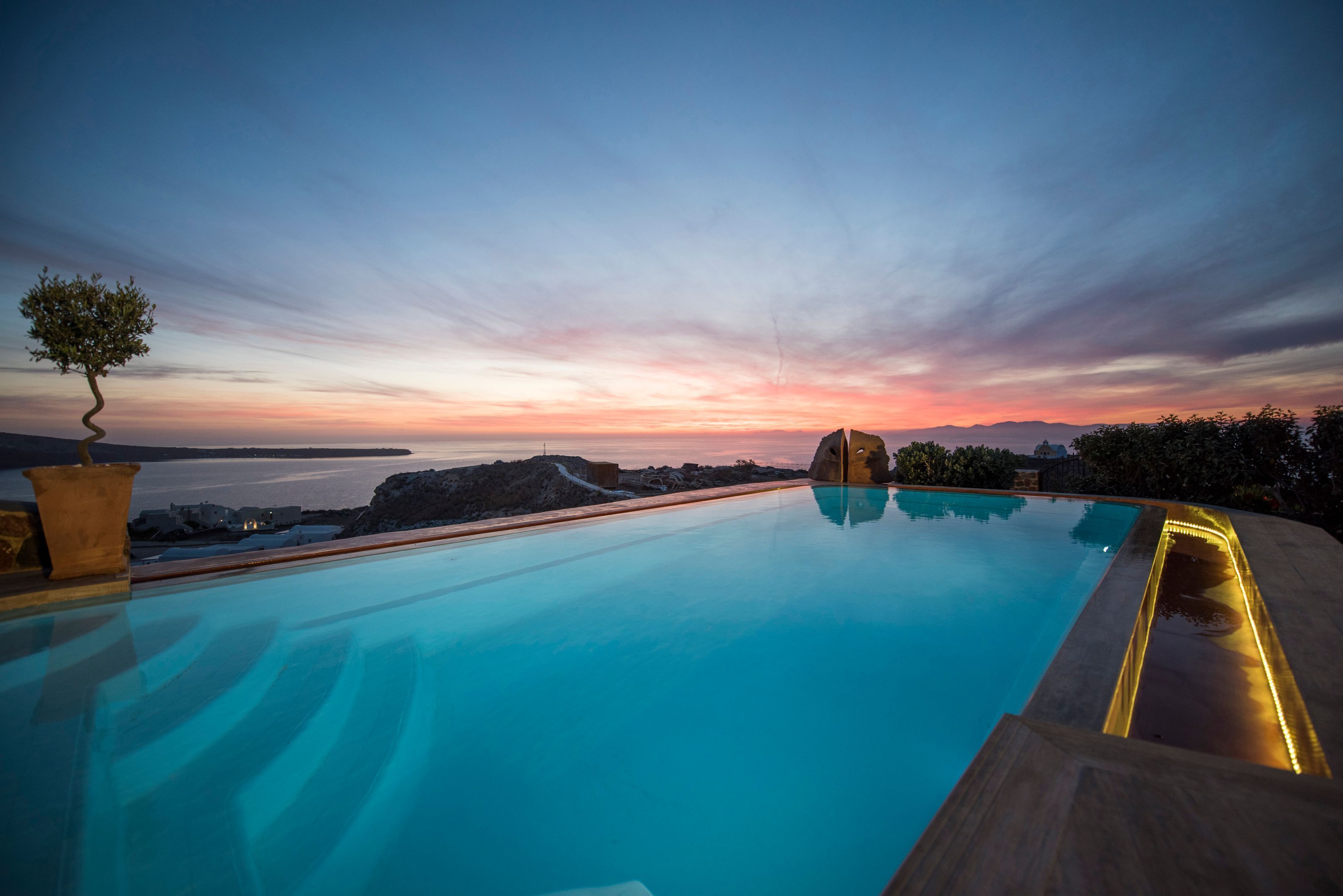 A pool with a sunset view, a tree, and a rocky landscape.