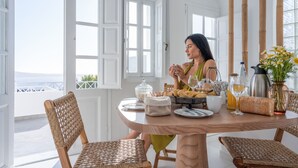 Comedor con vistas al mar, con sillas de mimbre, una mesa redonda y diversos productos para el desayuno.