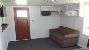 A small, compact room with a brown sofa, a grey carpet, a wooden door, and a window. - Meadow Cabin (Meeker)