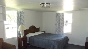 A bedroom with a bed, a nightstand with a lamp, a chair, and patterned curtains. - Meadow Cabin (Meeker)