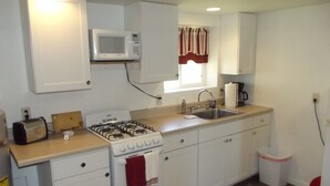 A compact kitchen with white cabinets, a gas stove, a microwave, and a sink. - Meadow Cabin (Meeker)
