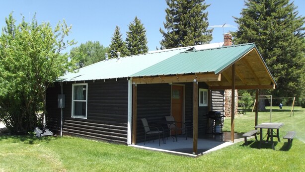 A log cabin with a covered porch, outdoor seating, and a stone chimney. - Meadow Cabin (Meeker)