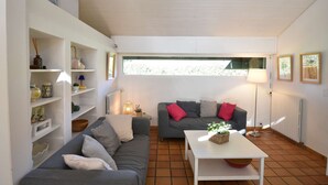 Ein Wohnzimmer mit grauem Sofa, weißen Regalen, einem weißen Tisch und einem Fenster mit Blick.