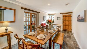 A dining area with a long wooden table set for four, flanked by wooden chairs, a wooden bench, and a wooden door.