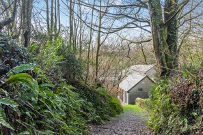 A narrow path leading to a rustic building surrounded by dense foliage and trees.
