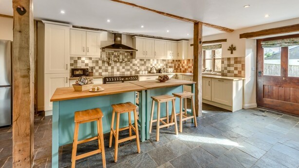 A kitchen with a central island, wooden stools, and a checkered backsplash.