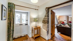 A hallway with a wooden door, a small table with a lamp, and a stone wall.