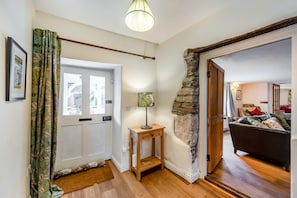 A hallway with a wooden door, a small table with a lamp, and a stone wall.