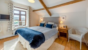 A bedroom with a large bed, two bedside tables, a chair, a TV, and a window with curtains.