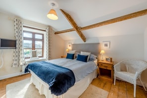 A bedroom with a large bed, two bedside tables, a chair, a TV, and a window with curtains.