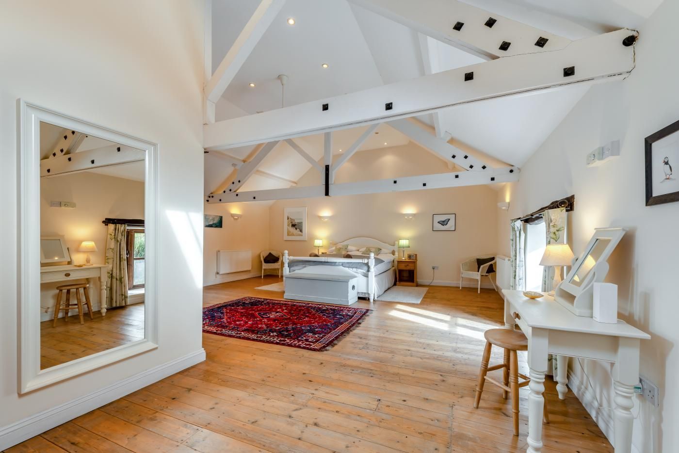 A spacious loft bedroom with a large bed, a sitting area with a desk, and a view of the outdoors.