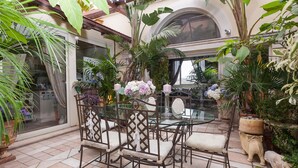 A glass-top table with four chairs, surrounded by potted plants and a decorative elephant statue. - Winter Garden - NAVONA SQUARE (Roma)