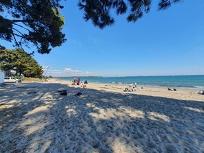 A beach with people sunbathing and swimming, a parked car, and a clear blue sky.